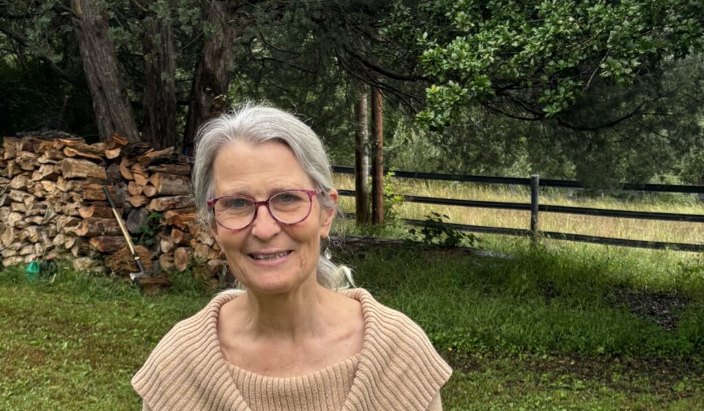 A portrait of owner Sallie Smithwick, a licensed acupuncturist, smiling in outdoors with trees in the background.